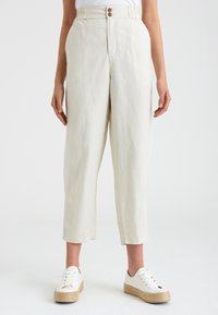 Linné, ljusbeiga byxor med avslappnad passform, elastisk midja och tvåknäppning, tillsammans med vita sneakers på en vävd plattform.