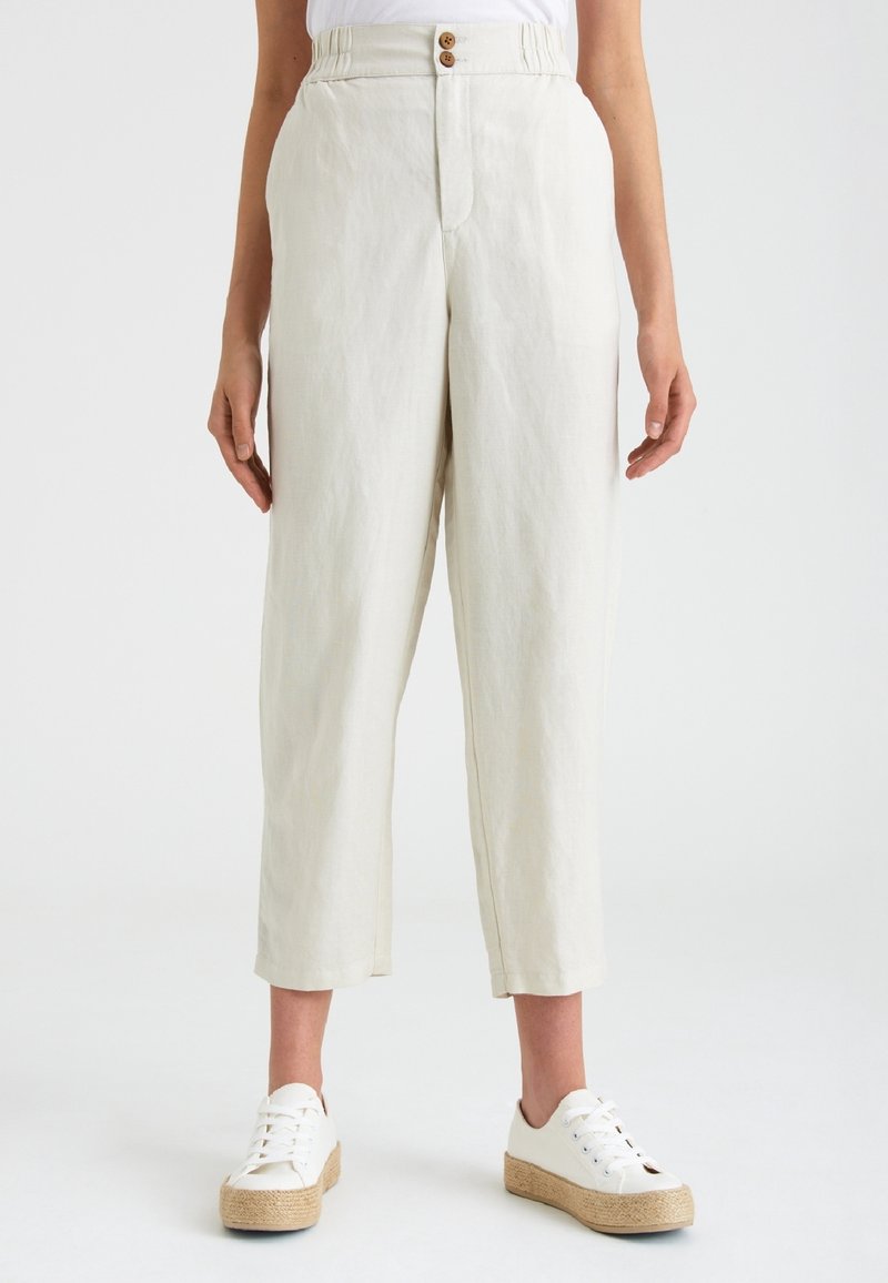 Linné, ljusbeiga byxor med avslappnad passform, elastisk midja och tvåknäppning, tillsammans med vita sneakers på en vävd plattform.