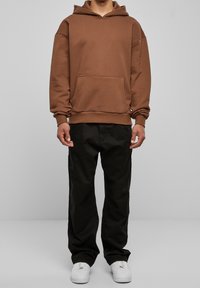 Brun luvtröja med ficka fram, ihop med svarta byxor och vita sneakers. Avslappnad passform och mjukt, texturerat tyg.