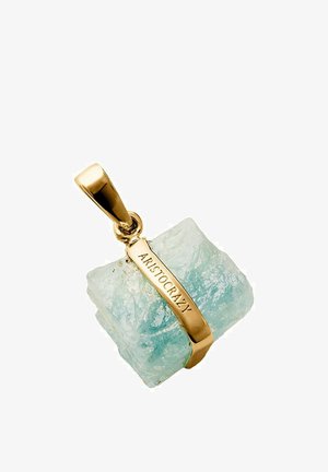 Colgante de oro que sostiene una piedra preciosa rugosa de color azul claro con "ARISTOCRAZY" grabado en la correa de metal.