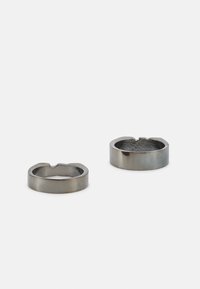 Anéis de metal em cinza escuro com um exterior liso. Um apresenta um design em forma de recorte entalhado, enquanto o outro possui uma superfície interior texturizada.