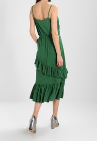 Green polka dot dress with a tiered ruffle hem, adjustable spaghetti straps, and a cinched waist. Paired with silver high-heeled shoes.