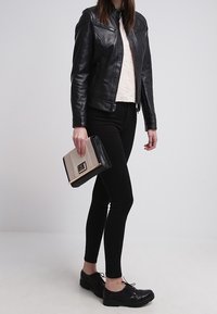 Černá kožená motorkářská bunda, světle texturovaný top, černé skinny džíny, černé šněrovací boty, držící béžovou a  černou kabelku s klopou.