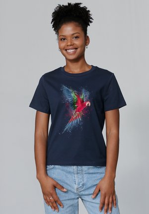 T-shirt en coton bleu marine avec un graphique coloré d'un perroquet aux ailes vertes et au corps rouge, sur un fond éclaboussé.