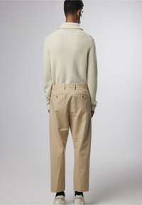 Pull en maille épaisse avec un large col, associé à un pantalon beige tailleur. Design simple, avec poches latérales et arrière, et des baskets.