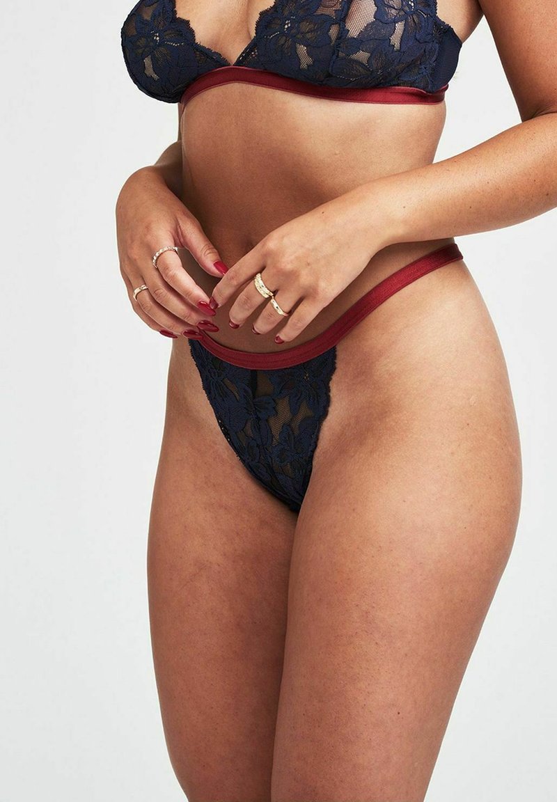 Kant lingerie set met een marinebloemig patroon en rode accenten. De bralette heeft dunne bandjes, terwijl de thong een doorschijnend zijpaneel heeft.