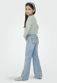 Gestreepte top met lange mouwen in wit en groen, gecombineerd met lichtblauwe klokjeans. De jeans hebben een klassieke vijf-pocket stijl.
