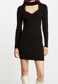 Robe noire en tricot côtelé à manches longues, avec un décolleté en V profond et un col choker. Possède une silhouette ajustée et des bordures argentées contrastantes.