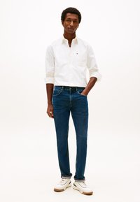 Valkoinen raidallinen paita, siniset farkut ja valkoiset tennarit. Slim fit -malli. Farkuissa on klassinen viisitaskurakenne ja näkyvät saumausta korostavat yksityiskohdat.