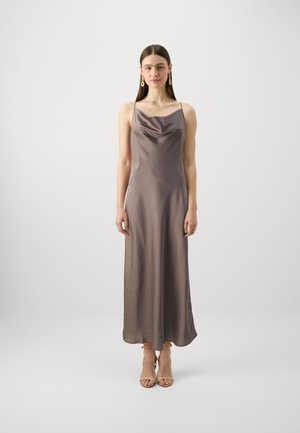 Robe maxi en satin taupe avec des bretelles fines et un col drapé, présentant une texture lisse qui se termine par un ourlet doux, accompagnée de sandales à talons beiges.