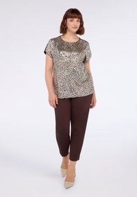 Top de manga corta en lentejuelas plateadas y beige con escote redondo, combinado con pantalones marrones ajustados y zapatos de tacón beige.