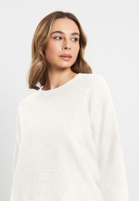 Witte trui met een subtiele glans, ronde hals en lange mouwen. Zachte textuur en een relaxte pasvorm, geschikt voor casual draag.
