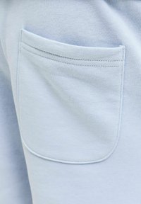 Tissu bleu clair avec une poche plaquée cousue avec double surpiqûre sur un matériau texturé.