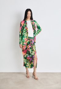 Barevná květinová souprava s bundičkou a sukní v zelené, růžové a fialové barvě. Sukně má řasení a vysoký rozparek, doplněná o podpatky.