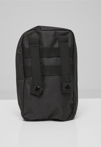 Bolsa compacta de nylon negro con dos correas verticales y botones de presión, diseñada para sujetarse a bolsas más grandes o cinturones.