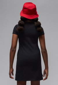 Fekete rövid ujjú ruha, testhezálló fazonnal, piros vödörkalappal párosítva. A ruha egyszerű, sima textúrájú.