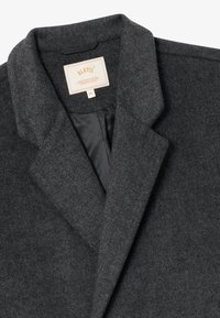 Blazer en laine gris foncé avec col à revers et doublure intérieure noire, affichant une étiquette de taille XL portant la marque BLKVIS.