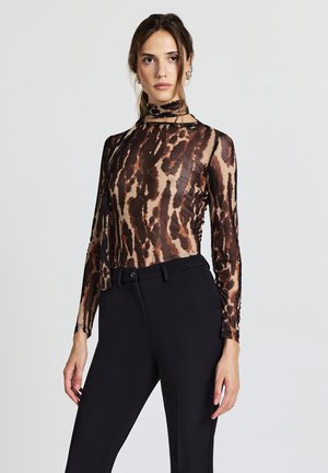 Haut transparent à manches longues avec un col montant, présentant un motif animalier marron et beige. Un pantalon noir moulant complète la tenue.