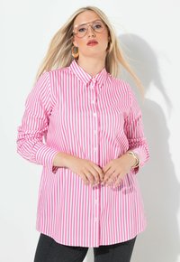 Gestreepte shirt in roze en wit, met knopen, lange mouwen en afgeronde zoom. Model draagt gouden accessoires met een gladde stoftextuur.