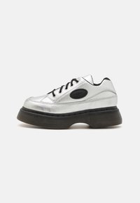 Srebrne skórzane sneakersy z czarnymi sznurowadłami, okrągłym noskiem i grubą gumową podeszwą. Mają charakterystyczną naszywkę z logo na boku.