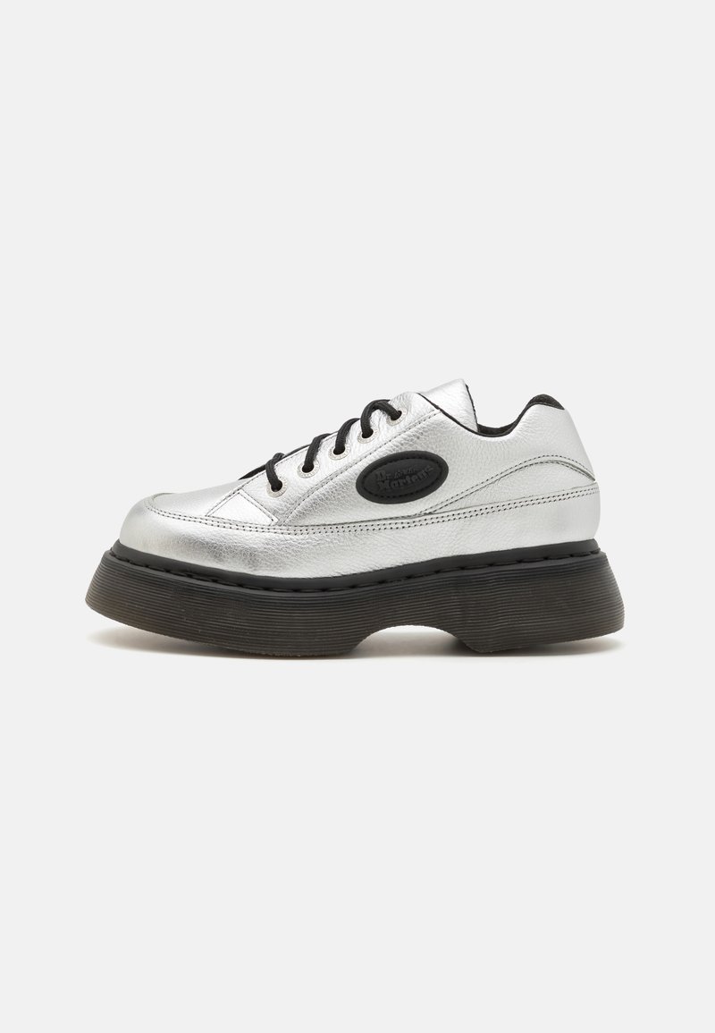 Zilveren leren sneaker met zwarte veters, een ronde neus en een dikke rubberen zool. Heeft een kenmerkende logo-opdruk aan de zijkant.