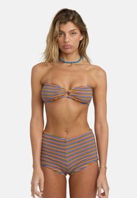 Csíkos bikini szett kék, narancssárga és zöld színekben. A bandeau felsőrész csavart elemmel és kivágással rendelkezik; a szoknyás alsó rész magasított derékkal. Simított textúra.