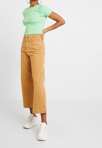 Lichtgroene geribde T-shirt met korte mouwen, gecombineerd met hoog- taille beige wijde broek. Model draagt witte sneakers. Eenvoudig ontwerp, effen kleuren.