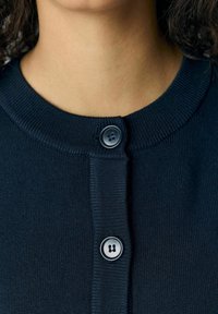 Cardigan en tricot bleu marine avec un col rond, deux fermetures à boutons noirs et une texture côtel�ée le long des poignets et de la patte de boutonnage.