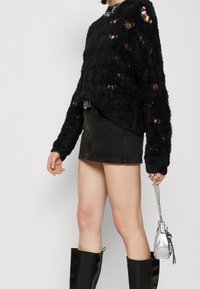 Pull en peluche noir avec de grandes découpes, associé à une mini-jupe en denim noir. Les accessoires comprennent un sac argenté et des bottes noires montantes.