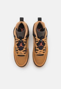 Paire de baskets montantes marron et noires avec des lacets couleur beige et des logos Jumpman rouges sur des languettes noires, vues de dessus sur fond blanc.