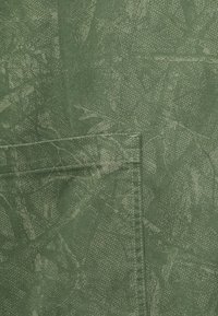 Πράσινο ύφασμα με σχέδιο φύλλου, που διαθέτει μια ξεχωριστή τσέπη και υφή με διακριτή επιφάνεια. Ορατά ραμμένα άκρα, που ενισχύουν την ανθεκτικότητα.