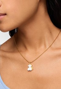 Collier en perles dorées avec un pendentif en forme d'ours blanc, présentant une texture lisse et un fond rehaussé de doré, mettant en évidence des éléments de design ludiques.