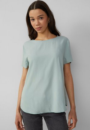 Chemise à manches courtes bleu clair avec un col rond, présentant une texture lisse et douce et un ourlet légèrement arrondi.