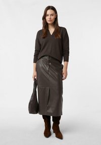 Brązowy sweter dzianinowy z dekoltem w serek, zestawiony z brązową skórzaną spódnicą midi z przednim rozcięciem, ciemnobrązową torebką na ramię oraz brązowymi zamszowymi botkami.