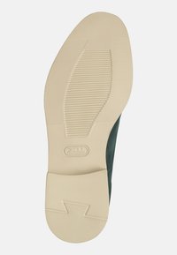 Suola in gomma con grip testurizzato, colore crema; tomaia verde scuro con finitura liscia e forma arrotondata; dettaglio del logo sulla suola.