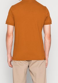 Spalony pomarańczowy bawełnowy t-shirt z krótkimi rękawami, okrągłym dekoltem i prostym dołem. Posiada małą metkę marki na dole po lewej stronie.