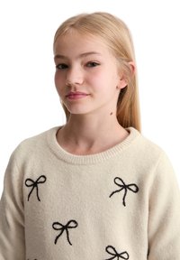 Maglione color crema con applicazioni a forma di fiocco nero, scollatura rotonda e maniche lunghe, realizzato in tessuto a maglia strutturato.