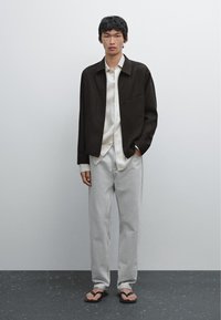 Mørkebrun jakke, hvid skjorte med knapper, lysegrå jeans og sorte klipklapper. Simpelt design med en afslappet pasform.