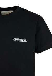 T-shirt in cotone nero con collo a giro e maniche corte. Presenta un logo bianco "ANOTHER COTTON" stampato sul petto. Textura liscia.