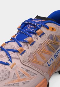 Chaussure de sport rose pâle et bleue avec des lacets bleus, des accents orange, des panneaux en mesh et le logo "La Sportiva" sur le côté.