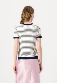 Top de manga corta a rayas en crema y azul marino. Presenta un cuello y puños acanalados, con un corte ajustado. Tejido suave con una textura lisa.