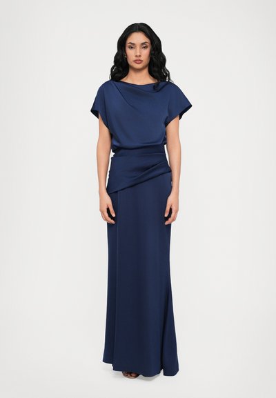 Robe longue bleu marine avec un col drapé et des manches chauve-souris courtes. Texture lisse et mate et taille cintrée, elle descend en jupe droite.