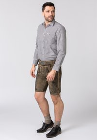 Herren karierte Hemd in Schwarz und Weiß, kombiniert mit brauner Lederkurz Hose mit floralem Stickmuster und einer dekorativen Gürtelschnalle, getragen mit grauen Socken und schwarzen Schuhen.