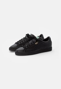 Zapatillas de cuero negro con un acabado suave, punta redonda, suela de goma texturizada y cordones negros. Presentan una etiqueta de marca verde en la lengüeta.