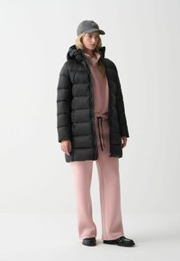 Schwarze puffige Jacke mit Kapuze, rosafarbener Reißverschluss-Sweatshirt und lockere rosa Hose. Eine graue Mütze und schwarze Schuhe vervollständigen den Look.