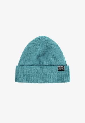 Gebreide beanie in teal met een opgevouwen omslag. Heeft een gestructureerd ribbelpatroon en een zwart label met witte tekst aan de zijkant.