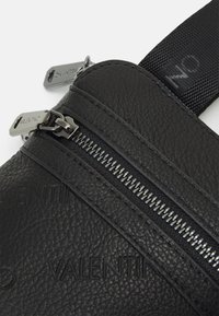 Černá kožená taška s dvěma kapsami na zip, texturovaným povrchem a kovovými doplňky, na přední straně s vyraženým nápisem "VALENTINO".