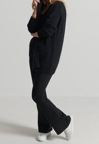 Svart, stickad kavaj med långa ärmar, öppen front och knytning i midjan. Kombinerad med utsvängda svarta byxor och vita sneakers.