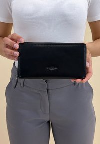 Zwart leren portemonnee met een gladde textuur, ritssluitingen en een reliëflogo op de voorkant. Heeft een rechthoekige vorm en wordt in handen weergegeven.
