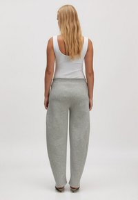 Grijze sweatpants van zacht materiaal, met een losse pasvorm, elastische tailleband en zijnaaddetails. Gepaard met een wit tanktop.